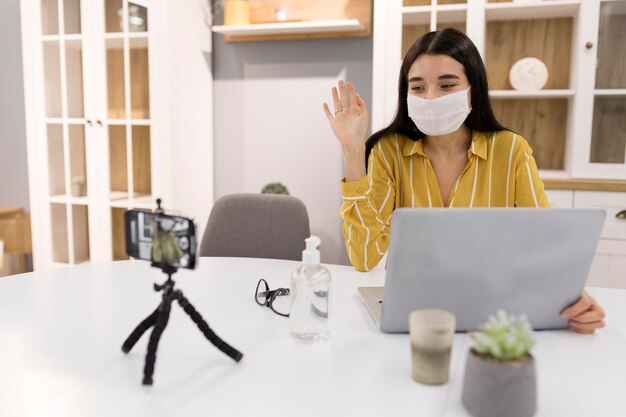 Vrouwelijke vlogger thuis met smartphone en medisch masker