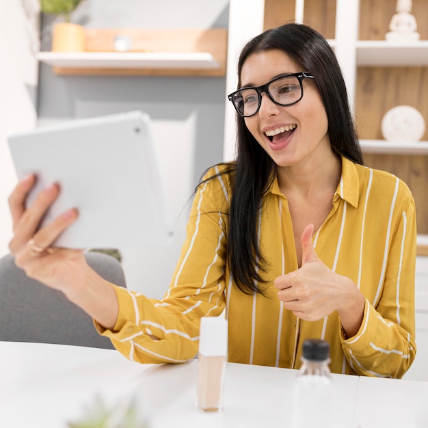 Gratis foto vrouwelijke vlogger thuis met tablet duimen opgevend