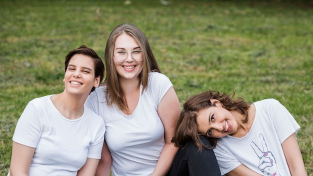 Gratis foto vrouwelijke vrienden die bij gras het glimlachen zitten
