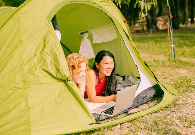 Vrouwelijke vrienden die in tent met laptop liggen