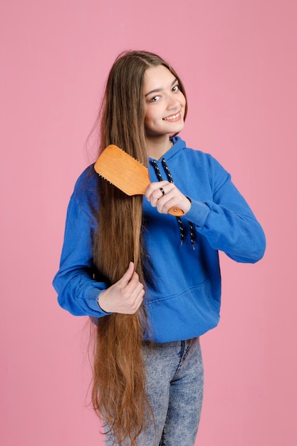 Vrouwelijke vrouw die heel lang sterk blond haar borstelt met houten haarborstel terwijl ze naar de camera glimlacht