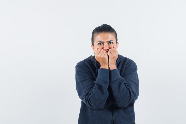 Vrouwelijke vuisten emotioneel bijten in hoodie en bang op zoek. vooraanzicht.