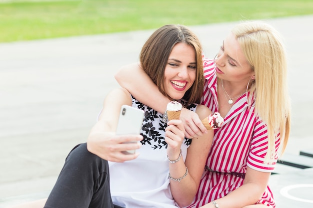 Vrouwelijke zitting met haar vrienden die selfie met mobiele telefoon nemen