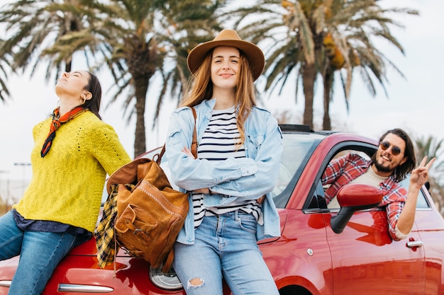 Gratis foto vrouwen dichtbij mens die uit auto leunen en vredesgebaar tonen