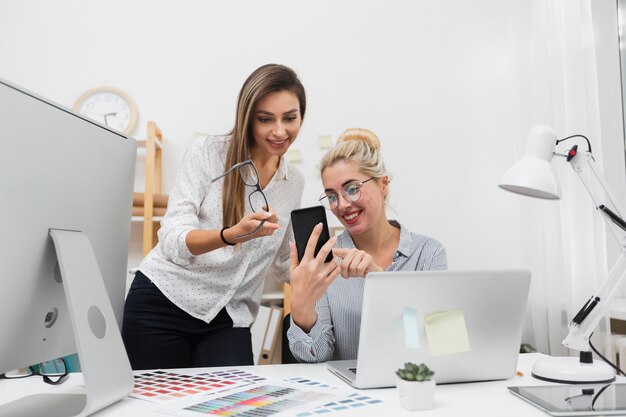 Vrouwen die op telefoon op kantoor kijken