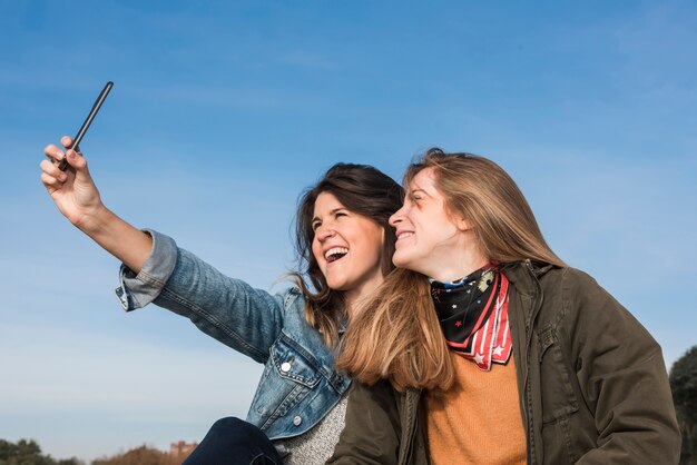 Vrouwen die selfie op blauwe hemelachtergrond nemen