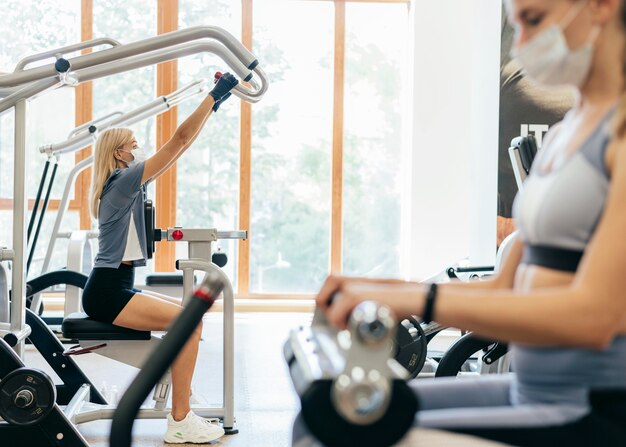 Vrouwen in de sportschool met behulp van apparatuur met medisch masker