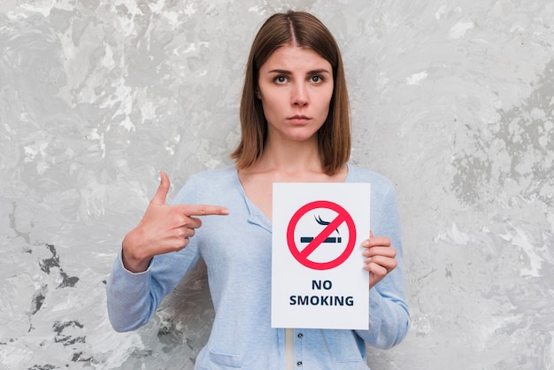 Gratis foto vrouwen wijzende vinger bij nr rokend poster die zich dichtbij doorstane muur bevinden