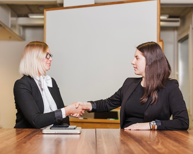 Vrouwen zitten aan tafel schudden handen