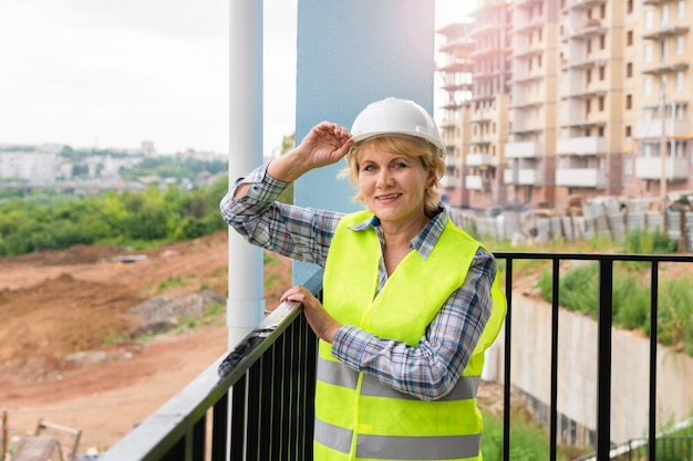 Vrouwenbouwer in een witte helm en een geel vest. vrouw die op middelbare leeftijd aan een bouwwerf werkt. ze houdt de helm in haar hand.