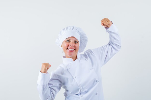 vrouwenchef-kok die winnaargebaar in wit uniform toont en gelukkig kijkt.