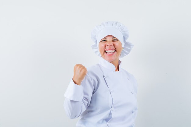 vrouwenchef-kok die winnaargebaar in wit uniform toont en gelukkig kijkt.