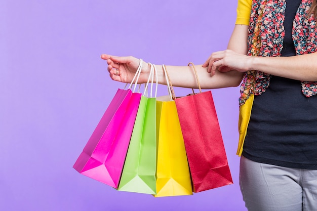Vrouwenhand die kleurrijke het winkelen zak op purpere achtergrond houden
