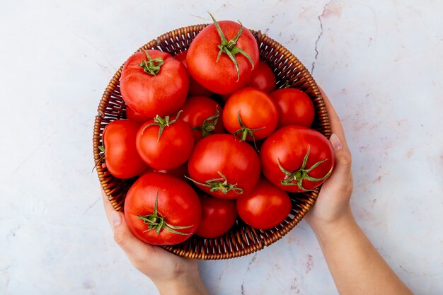 Vrouwenhanden die mand tomaten op witte oppervlakte houden