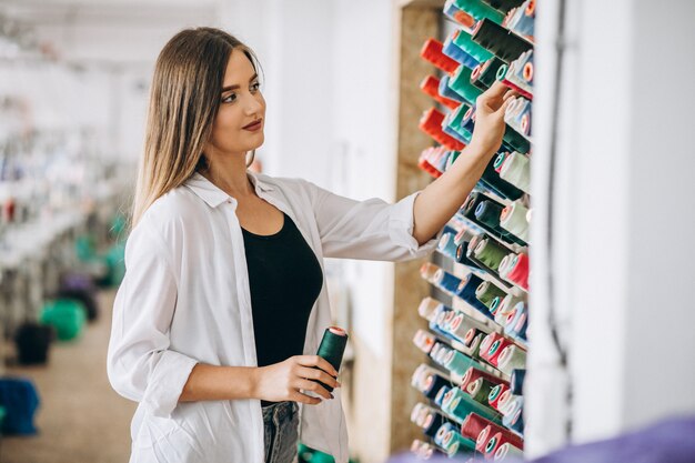 Vrouwenkleermaker die draden kiezen bij een fabriek