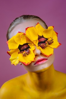 Vrouwenmodel met gele bloemen rond haar ogen. het lichaam van de vrouw is geel geverfd