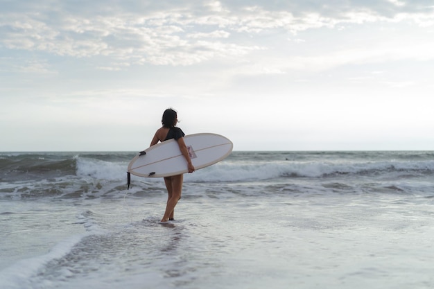 Vrouwensurfer met surfplank op de oceaan bij zonsondergang