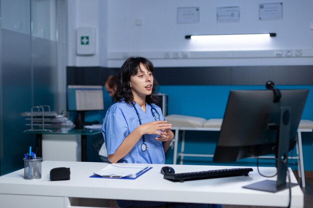 Vrouwenverpleegster die videogesprek met webcam op computer gebruikt voor gesprek op afstand, laat werken. Medisch assistent in gesprek met patiënt op online videoconferentie voor telezorg en consult