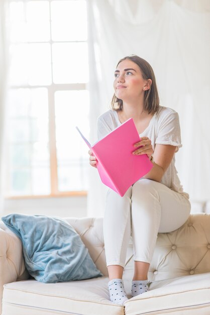 Vrouwenzitting bovenop bank die roze boek houden weg kijkend