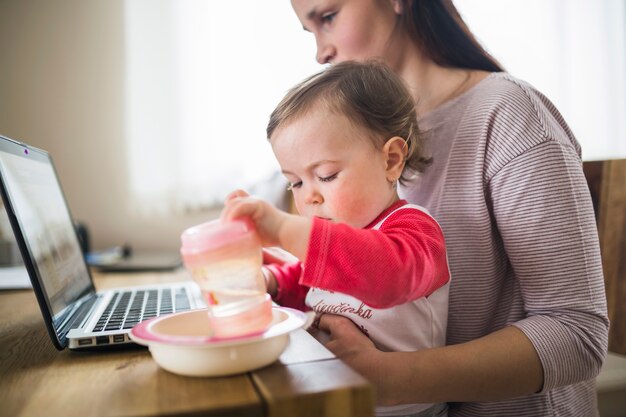 Vrouwenzitting met haar babymeisje die aan laptop werken