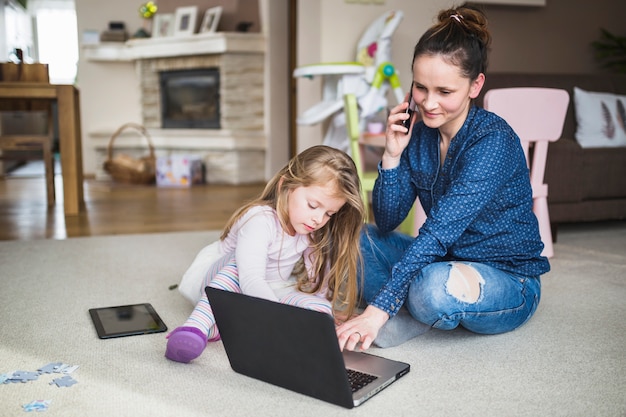 Vrouwenzitting met haar dochter die op cellphone spreken terwijl het gebruiken van laptop