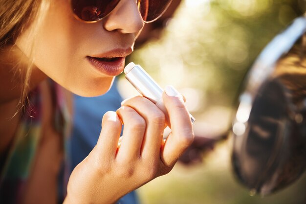 Vrouwenzitting op autoped die in openlucht make-up van lippen doen.