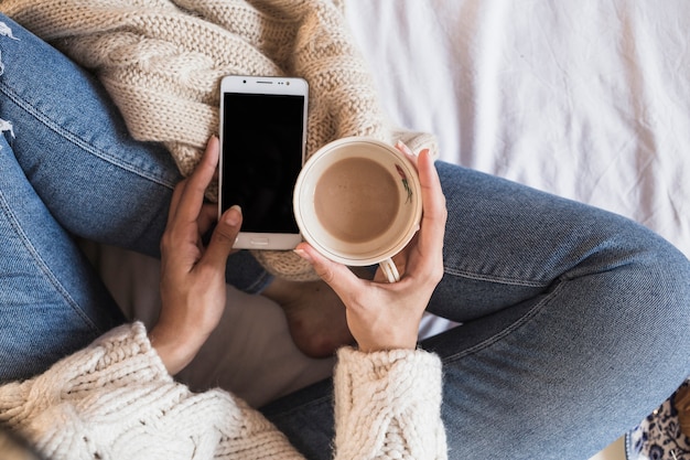 Vrouwenzitting op bed met smartphone en koffie