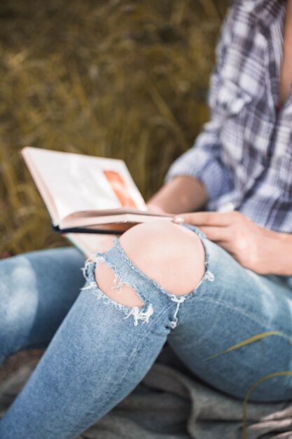 Vrouwenzitting op gras met boek in verontruste jeans