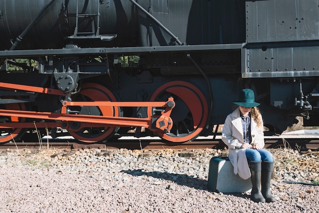 Gratis foto vrouwenzitting op koffer bij trein
