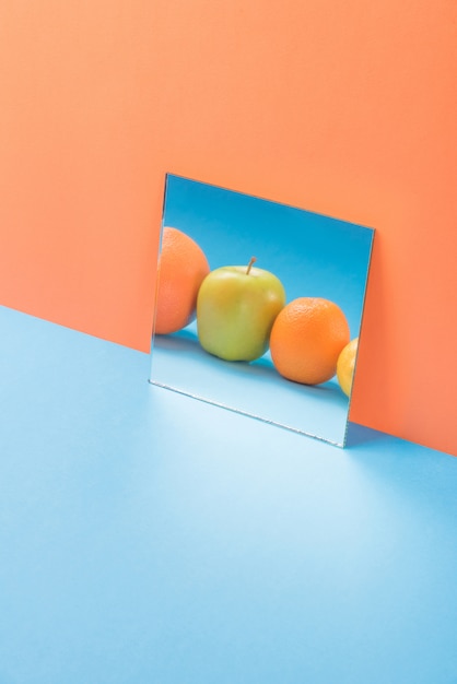 Gratis foto vruchten in spiegel op blauwe tafel geïsoleerd op oranje