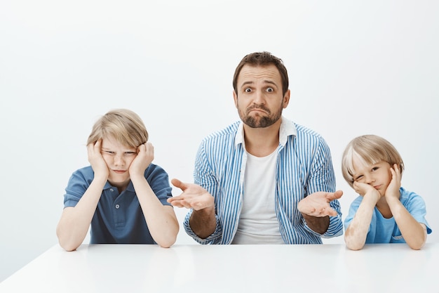 Waarom zonen zijn boos. Portret van clueless nerveuze schoonvader zitten met twee leuke jongens aan tafel