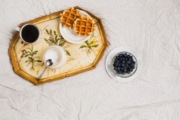 wafels; melkpot; koffiekopje en bosbessen kom op wit verfrommeld tafelkleed