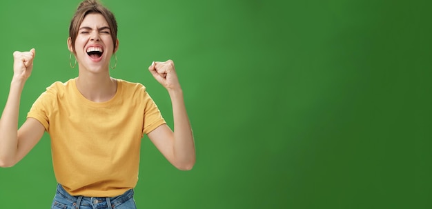 Waistup opname van charismatische energieke en opgewonden vrouw in geel t-shirt sluiten ogen schreeuwen van