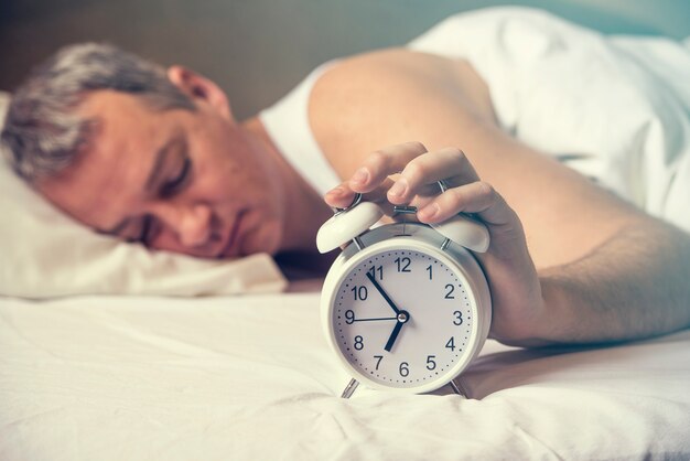 Wakker geworden. Hand schakelt de wekker uit in de ochtend. Zachte huidtoon. Uitgeputte man wordt wakker gewekt door een wekker in zijn slaapkamer