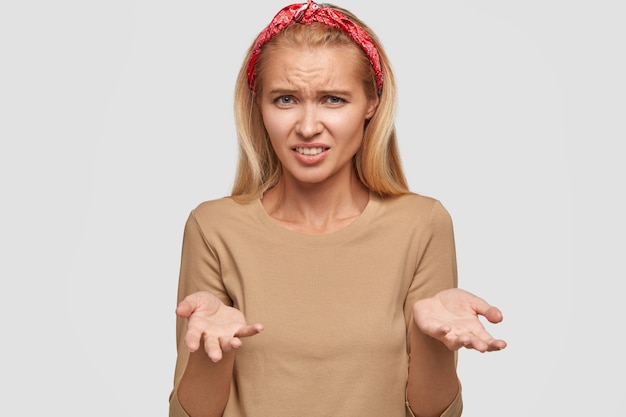 Wanhopige blonde jonge vrouw poseren tegen de witte muur