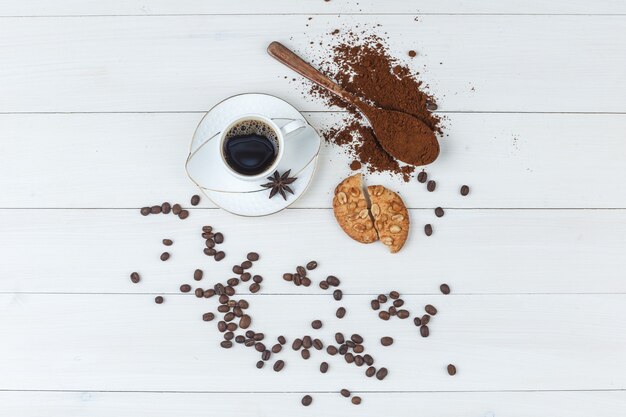 Wat koffie met gemalen koffie, kruiden, koffiebonen, koekjes in een kopje op houten achtergrond, plat leggen.