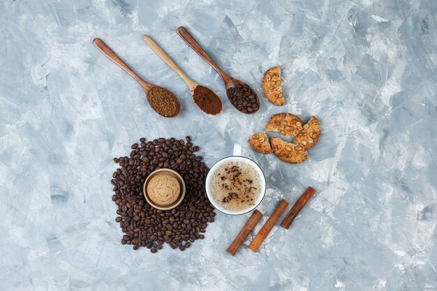 Wat koffie met koekjes, koffiebonen, gemalen koffie, kaneelstokjes in een kop op grungy grijze achtergrond, bovenaanzicht.
