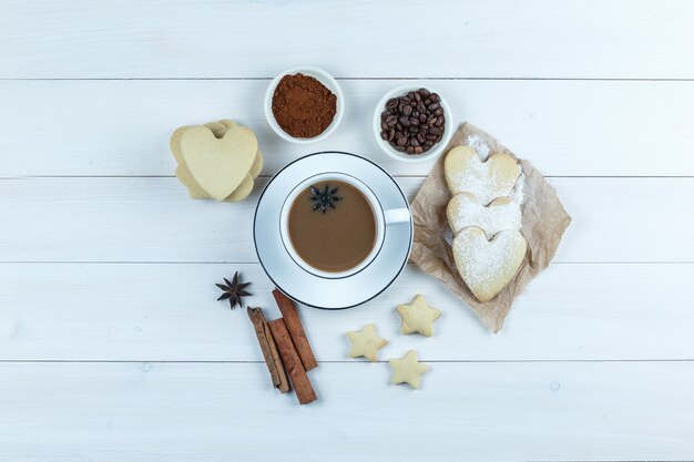 Wat koffie met koekjes, kruiden, koffiebonen, gemalen koffie in een kopje op houten achtergrond, bovenaanzicht.