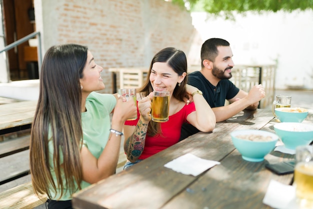 Wat roddels delen. Beste vrouwelijke vrienden praten bij over hun leven onder het genot van een drankje terwijl ze met hun groep vrienden rondhangen in een buitenbar