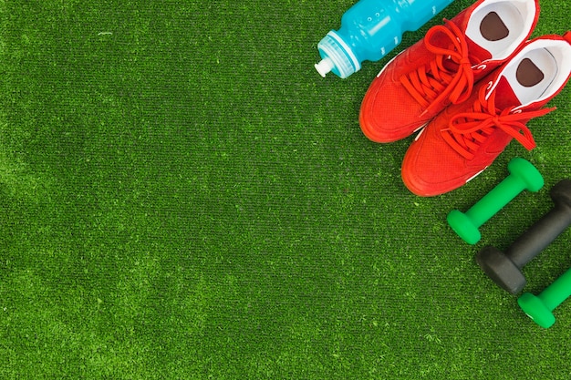 Waterfles; rode sportschoenen en halters op groen gras
