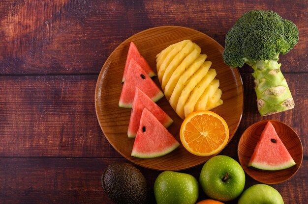 Watermeloen, ananas, sinaasappelen, in stukken gesneden met avocado, broccoli en appels op houten tafel. Bovenaanzicht.