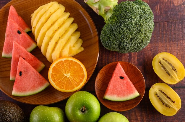 Watermeloen, sinaasappel, ananas, kiwi in plakjes gesneden met appels en broccoli op een houten plaat en houten tafel.