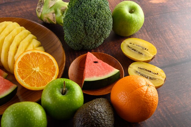 Watermeloen, sinaasappel, ananas, kiwi in plakjes gesneden met appels en broccoli op een houten plaat en houten tafel.