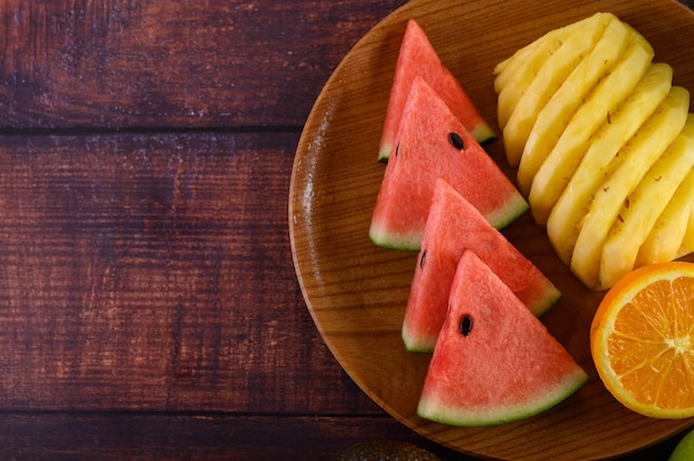 Watermeloen, sinaasappel en ananas in stukken gesneden op een houten plaat