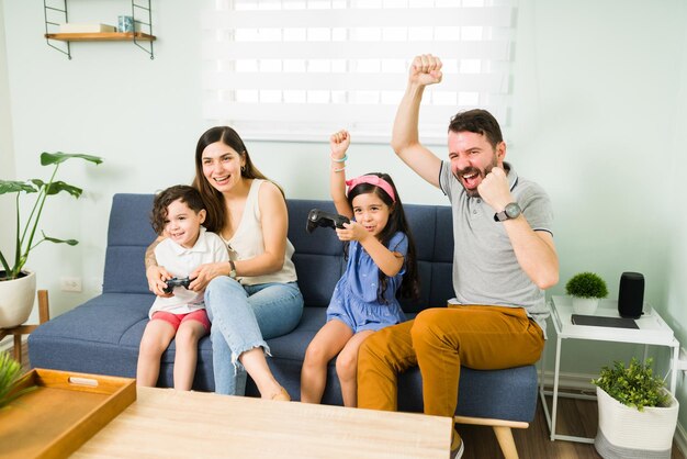 We zijn aan het winnen! Aantrekkelijke vader die een overwinning viert tijdens een videogame met zijn kinderen en familie