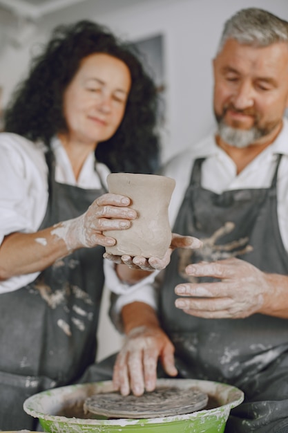 Wederzijds creatief werk. Volwassen elegant paar in vrijetijdskleding en schorten. Mensen maken een kom op een aardewerkschijf in een kleistudio.