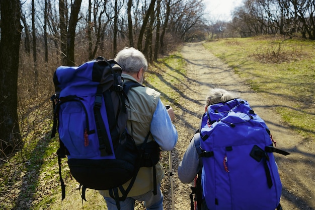 Weer klaar voor meer. Leeftijd familie paar man en vrouw in toeristische outfit wandelen op groen gazon in de buurt van bomen in zonnige dag. Concept van toerisme, gezonde levensstijl, ontspanning en saamhorigheid.