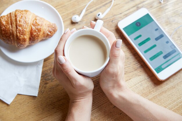 Weergave van bovenaf van vrouwelijke handen met een kopje koffie