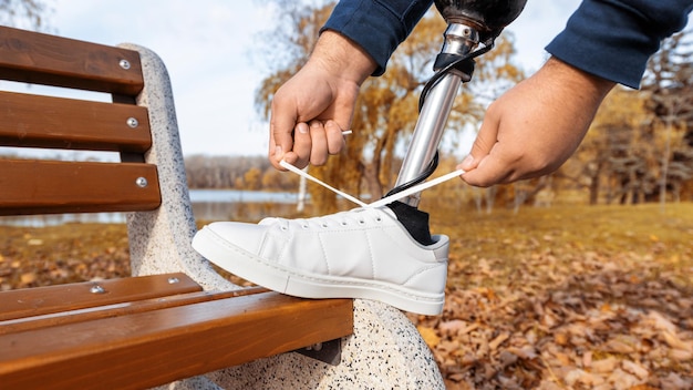 Gratis foto weergave van een man met prothetische benen en witte sneakers veters strikken met zijn voet op de bank