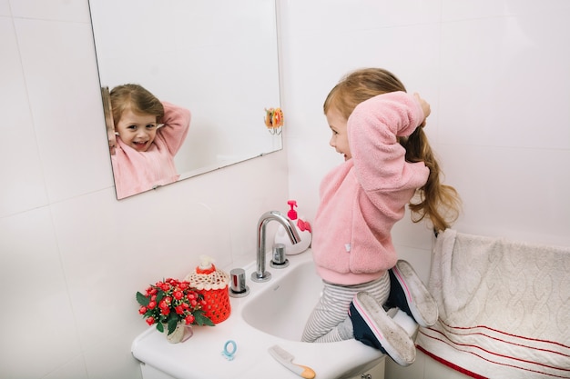 Weerspiegeling van een gelukkig meisje dat haar haar in spiegel bindt